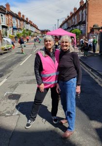 Cllr Kerry Jenkins at Moseley Festival's anniversary celebration, wearing a pink high vis jacket that is the same colour as a gazebo in the background.